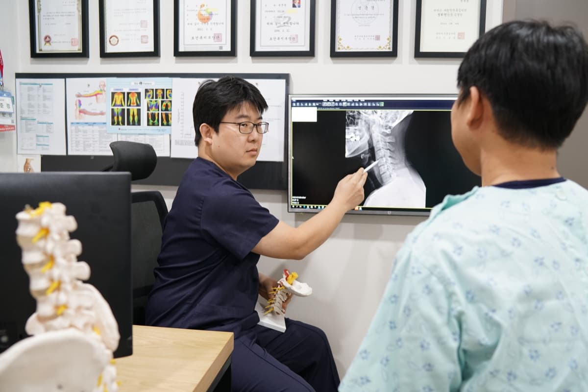 진료실에서 모니터의 X-ray 영상을 가리키며 환자에게 설명하는 모습