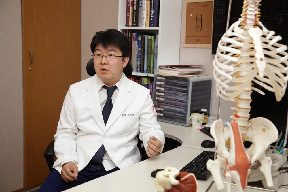 최승표 대표원장이 진료실에서 척추 모형을 두고 설명하는 모습