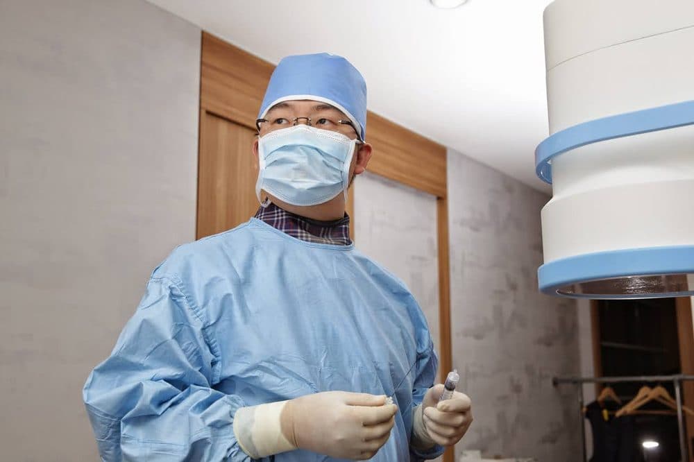 최승표 대표원장이 시술 가운을 입고 C-arm 옆에서 주사기를 든 모습